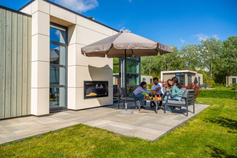 Familie nyder udendørs måltid ved ferieparkens glampingbolig med moderne design og stor parasol.