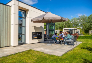 Familie nyder udendørs måltid ved ferieparkens glampingbolig med moderne design og stor parasol.