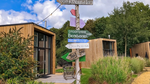 Foto bij een vakantiepark met moderne glampinghutten, kleurrijke wegwijzers en groene omgeving in de zon.
