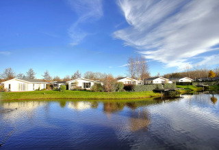 Afbeelding van een vakantiepark met glamping-accommodaties gelegen aan een vijver met blauwe lucht.