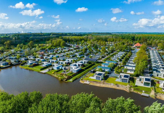 Luftfoto af en feriepark med moderne glampingboliger ved søbred og omgivet af grøn natur og skov.