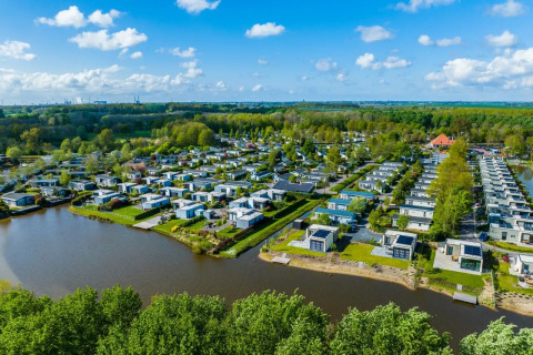 Aerial view of a holiday park with glamping lodges by a lakeside, surrounded by lush green forest.
