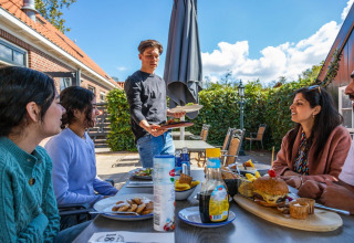 Gruppo di persone mangia all’aperto in un villaggio vacanze con sistemazioni glamping e sole.
