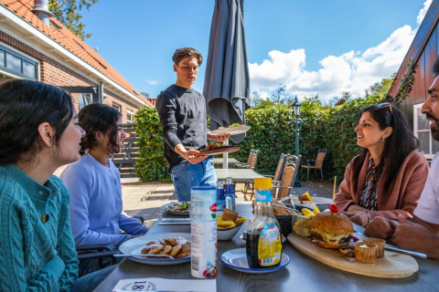 Grupo de personas disfruta de una comida al aire libre en un parque vacacional con alojamiento glamping.