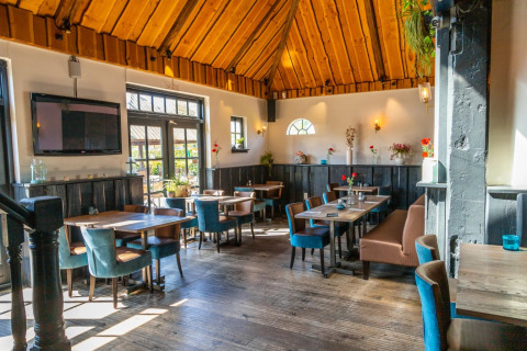 Salle de restaurant lumineuse dans un parc de vacances, avec plafond en bois et mobilier moderne.