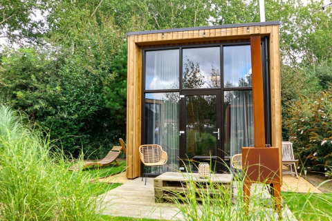 Glamping indkvartering i feriepark med moderne træhytte, havemøbler og grønne omgivelser.