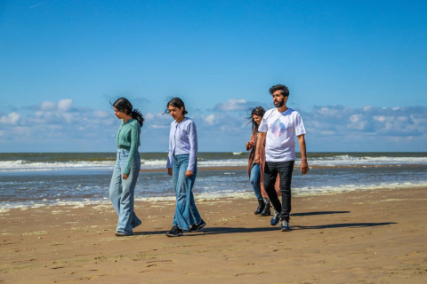 Vier mensen wandelen op het strand bij een vakantiepark met glamping, tijdens een zonnige dag aan zee.