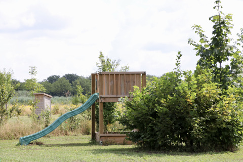 Ein Holzspielplatz mit grüner Rutsche, umgeben von Büschen im Ferienpark de Heerlijkheid Vorenseinde.