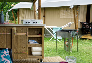 Area cucina all'aperto con barbecue e tenda safari al Camping La Dolce Vita nei Paesi Bassi.
