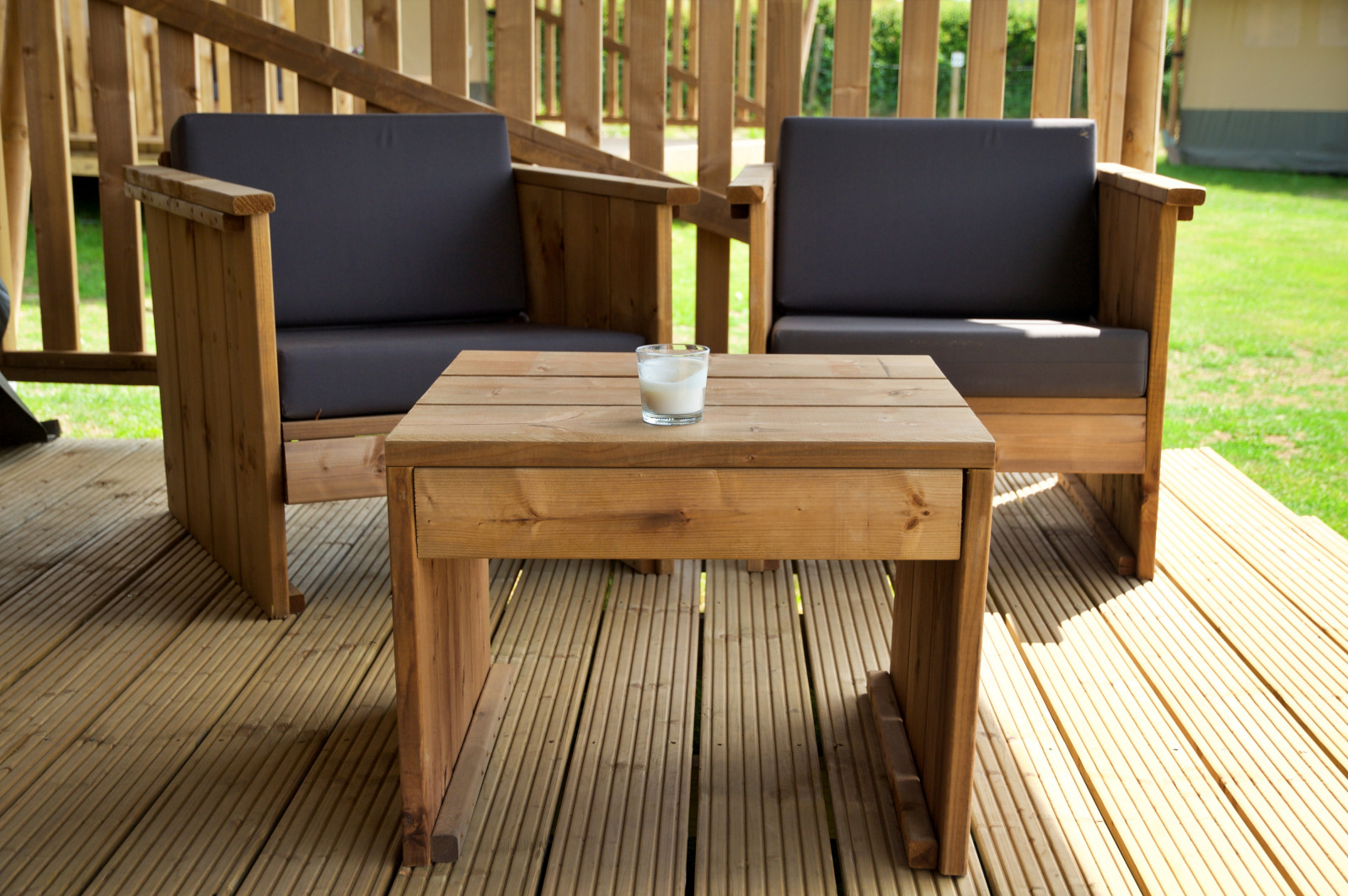 Tuinset van hout met twee stoelen en een tafel op een terras voor een safaritent in het zonlicht.