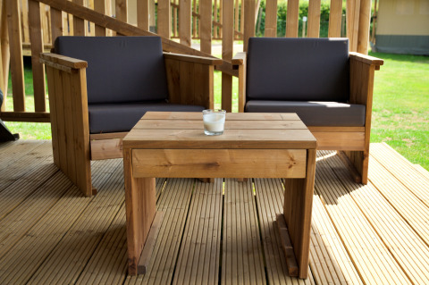 Wooden patio furniture set with two armchairs and a table on a deck outside a safari tent in daylight.