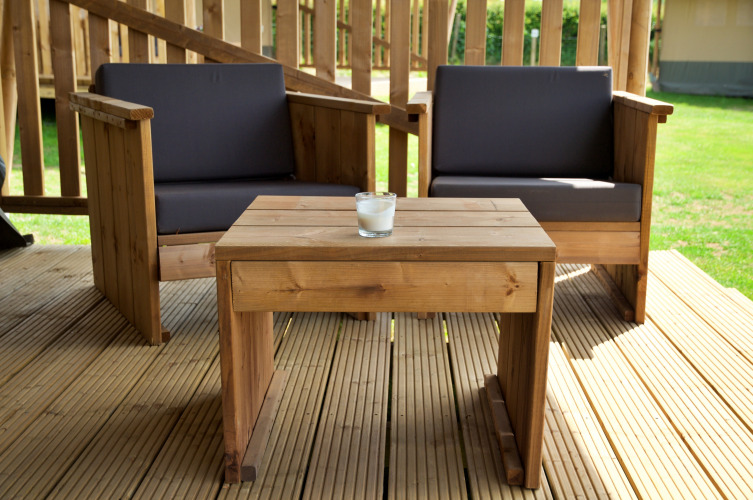 Salon de jardin en bois avec deux fauteuils et une table sur la terrasse d'une tente safari, en plein jour.