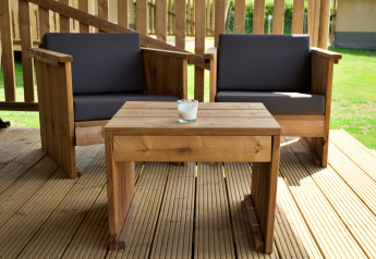 Salon de jardin en bois avec deux fauteuils et une table sur la terrasse d'une tente safari, en plein jour.