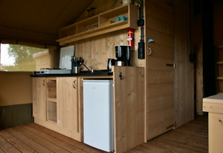 Vista interior de una tienda safari equipada con pequeña cocina de madera, estufa de gas y nevera compacta.