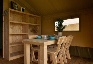 Mesa y sillas de madera en tienda safari con estantes y planta en Camping La Dolce Vita, Holanda.