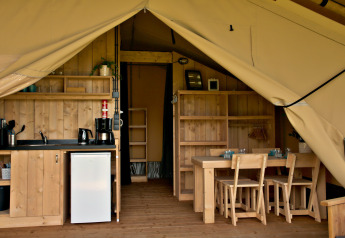 Binnenkant van een glampingtent met keukentje, koelkast, houten tafel en stoelen, gezellig ingericht.