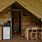 Interieur van een glampingtent met kitchenette, koelkast, houten eettafel en stoelen zichtbaar.