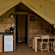 Indretning af luksustelt med lille køkken, spisebord, stole og træmøbler, typisk for glamping.