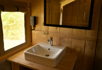 Lavabo moderno con espejo en una tienda safari, paredes de madera y luz natural entrando por la ventana.