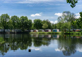 Vakantiepark met glampinghuisjes aan een meer, omringd door bomen en onder een blauwe lucht.