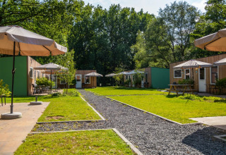 Panorama esterno di sistemazioni glamping in un villaggio vacanze con ombrelloni, prato e bungalow in legno.