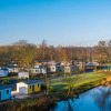 Holiday park with glamping accommodations, tiny cabins beside a scenic lake, surrounded by leafy trees.