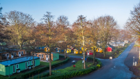Vista aérea de un parque vacacional con cabañas glamping coloridas, caminos y árboles a su alrededor.