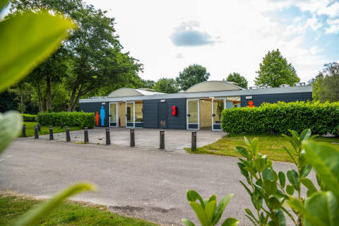 Et moderne servicehus med toiletter og brusere i en grøn feriepark, ideelt til glamping-gæster.