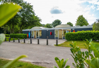 Et moderne servicehus med toiletter og brusere i en grøn feriepark, ideelt til glamping-gæster.