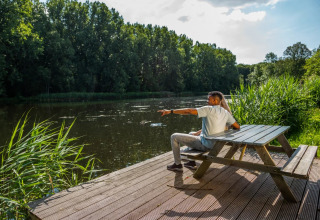Pareja sentada en un banco junto al lago en un parque de glamping, disfrutando del paisaje natural.