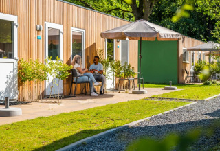 Un couple se détend devant des cabanes de glamping modernes dans un parc de vacances verdoyant et ensoleillé.