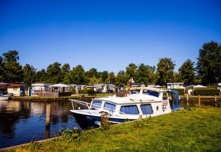 A boat docked by the shore of a lake at a holiday park in Friesland, Netherlands, with cabins and greenery.