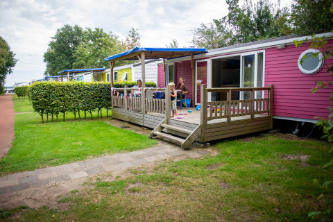 Family relaxing outside a colorful holiday cabin at Vakantiepark Bergumermeer in Friesland, Netherlands.