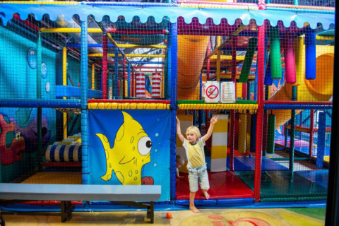 Bambino che gioca in un colorato parco giochi al coperto con scivoli e reti a Vakantiepark Bergumermeer, Paesi Bassi.