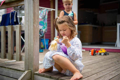 Meisje speelt met pop op het terras van een vakantiewoning in Vakantiepark Bergumermeer, Friesland, Nederland.