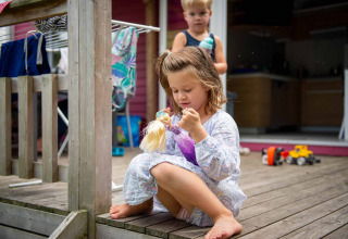 Mädchen spielt mit einer Puppe auf der Veranda eines Ferienhauses im Vakantiepark Bergumermeer, Friesland.