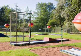 Minigolfbane i solrigt feriepark i Friesland, Holland, omgivet af grønt græs og træer.