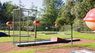 Campo de minigolf en parque vacacional soleado en Frisia, Países Bajos, rodeado de césped y árboles.