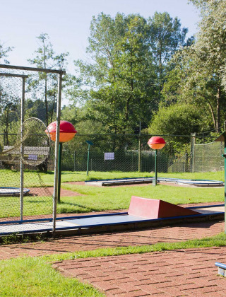Campo de minigolf en parque vacacional soleado en Frisia, Países Bajos, rodeado de césped y árboles.