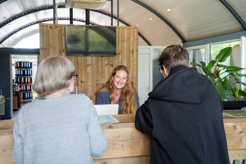 Recepcionista sonríe a dos huéspedes en Vakantiepark Bergumermeer, Friesland, Países Bajos.
