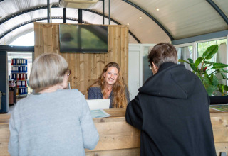 Receptionist smiler til to gæster ved skranken i Vakantiepark Bergumermeer, Friesland, Holland.