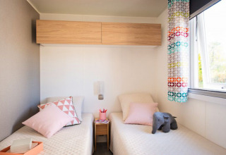 Moderne lodge-soveværelse med to enkeltsenge, pastel puder, farverige gardiner og stort vindue.