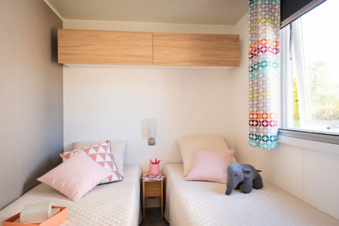 Dormitorio moderno de lodge con dos camas individuales, cojines pastel y cortina colorida junto a la ventana.