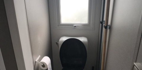 Kleines Badezimmer mit Toilettenschüssel, schwarzem Sitz, Fenster und Toilettenpapier in einer Lodge.