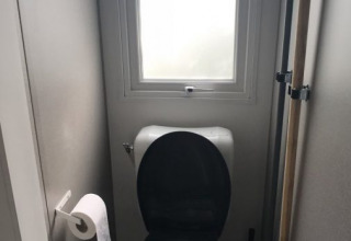 Kleines Badezimmer mit Toilettenschüssel, schwarzem Sitz, Fenster und Toilettenpapier in einer Lodge.