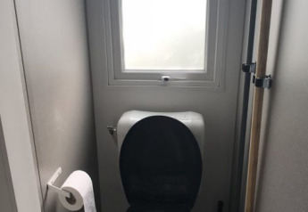 Compact bathroom with toilet, black seat, toilet paper, and window at Lodge XL in Vakantiepark Bergumermeer.