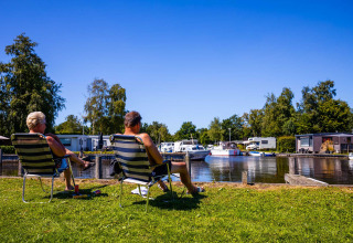 Zwei Menschen entspannen sich auf Stühlen am Wasser im Vakantiepark Bergumermeer, Friesland, Niederlande.