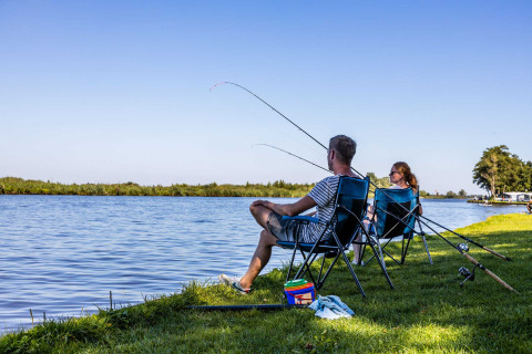 Deux personnes pêchent au bord du lac à Vakantiepark Bergumermeer, parc de vacances en Frise, Pays-Bas.