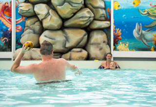 Mand, kvinde og barn leger i en indendørs pool med farverige havlivsmalerier, Vakantiepark Bergumermeer.