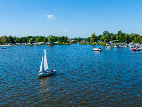 Velero en un lago cerca de Sumar, Frisia, Países Bajos, rodeado de árboles y barcos en el fondo